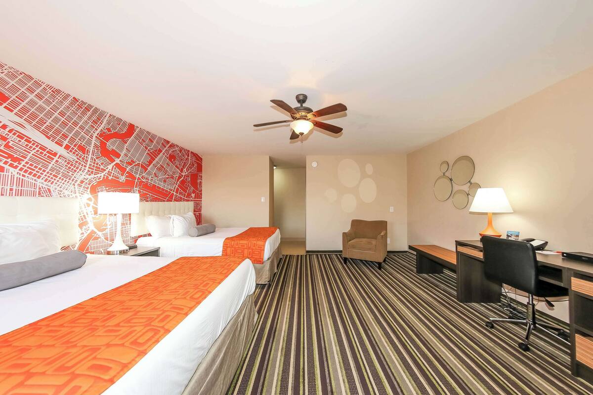 Quarto de hotel com cama, escrivaninha, cadeira, ventoinha no teto e um mapa na parede.