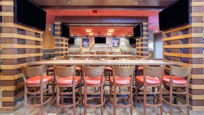 Een bar met houten lambrisering, meerdere televisies en rode fauteuils.