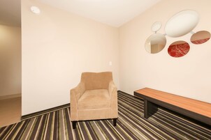 Una habitación con un sillón beige, un banco de madera y una alfombra estampada.