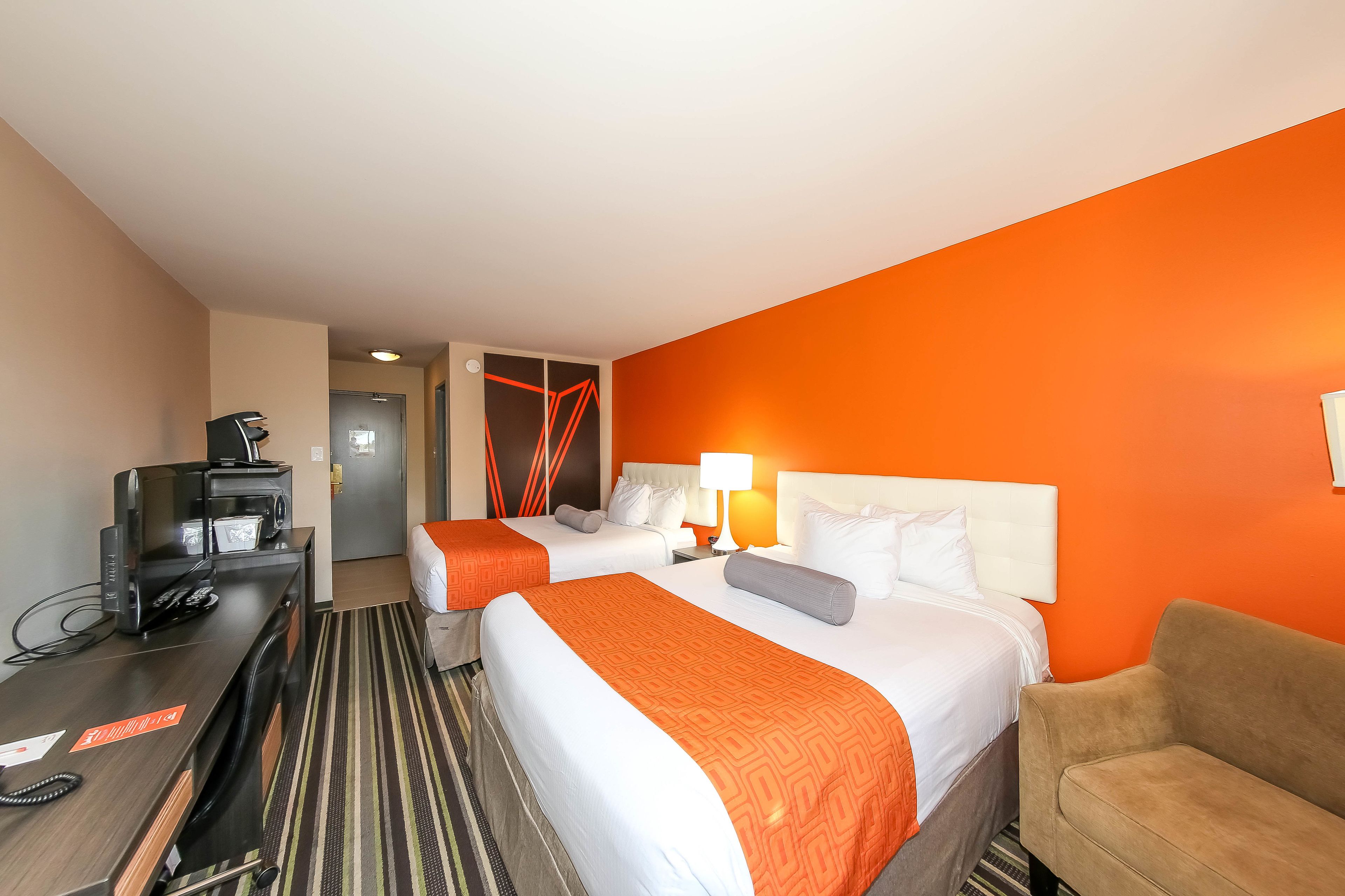 A hotel room with two beds, a desk with a telephone, a coffee machine, and a sofa.