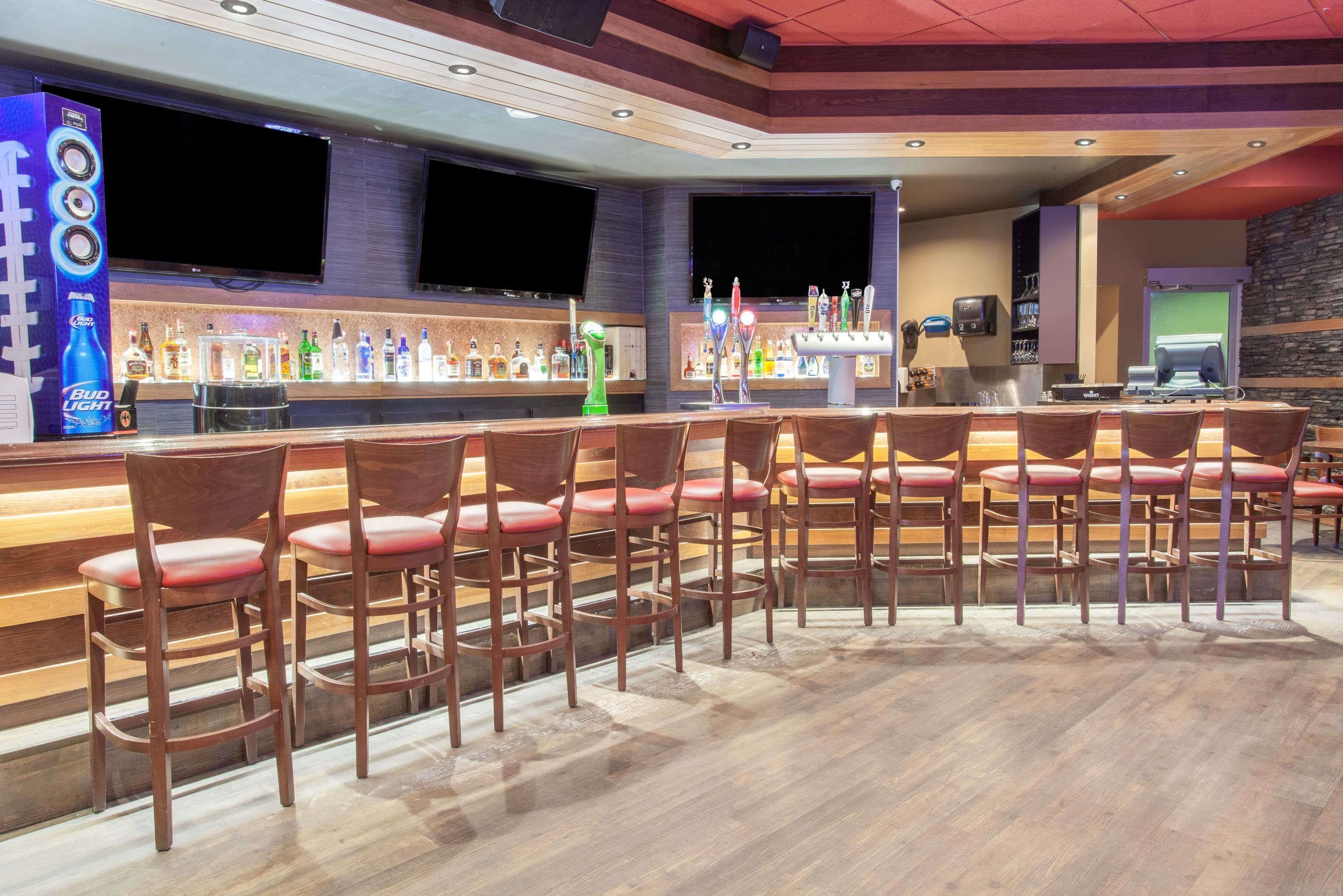 A bar area with multiple stools, a bar counter with various bottles, and a television screen mounted on the wall.