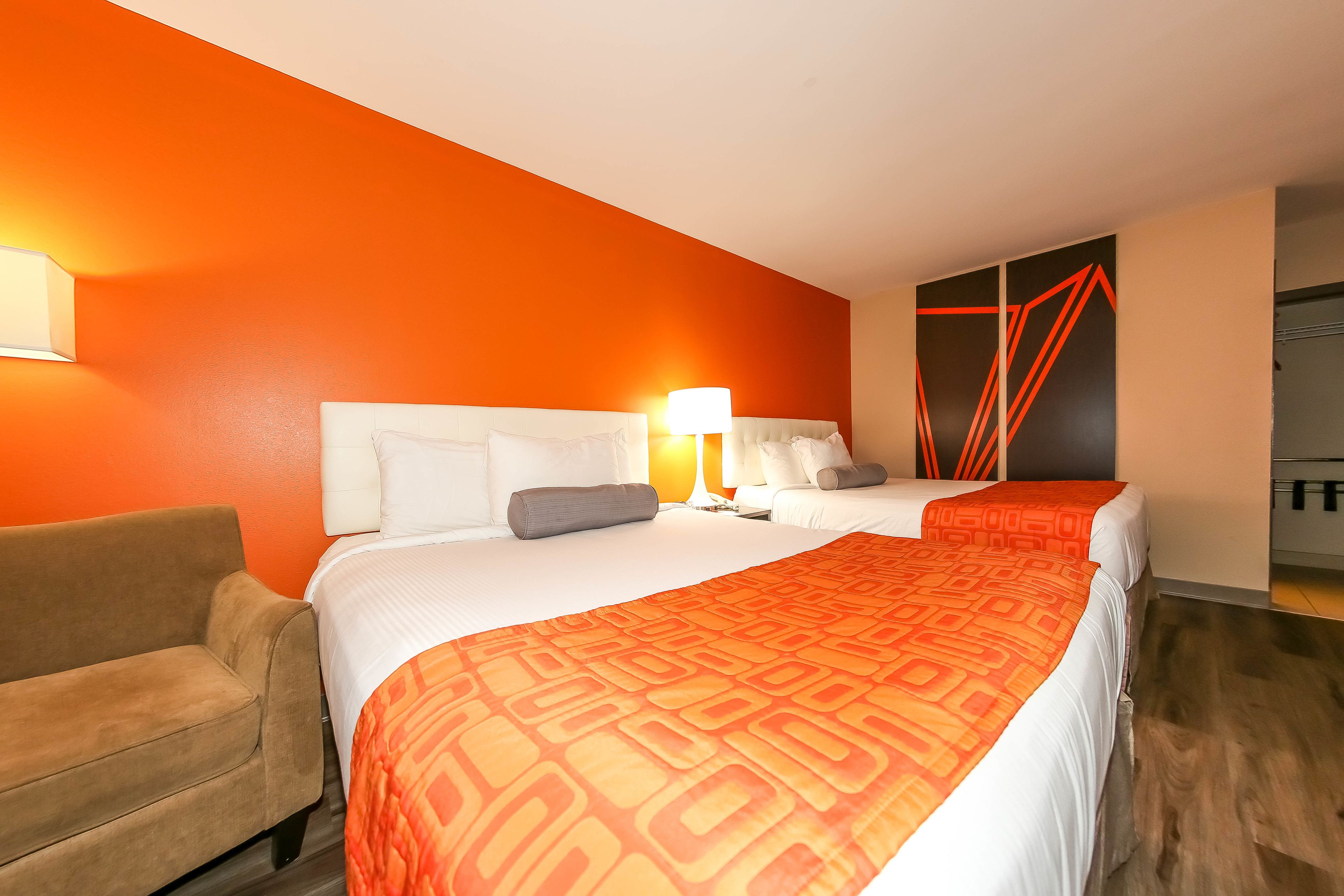 Ett hotellrum med två sängar, en soffa och en knallorange vägg.