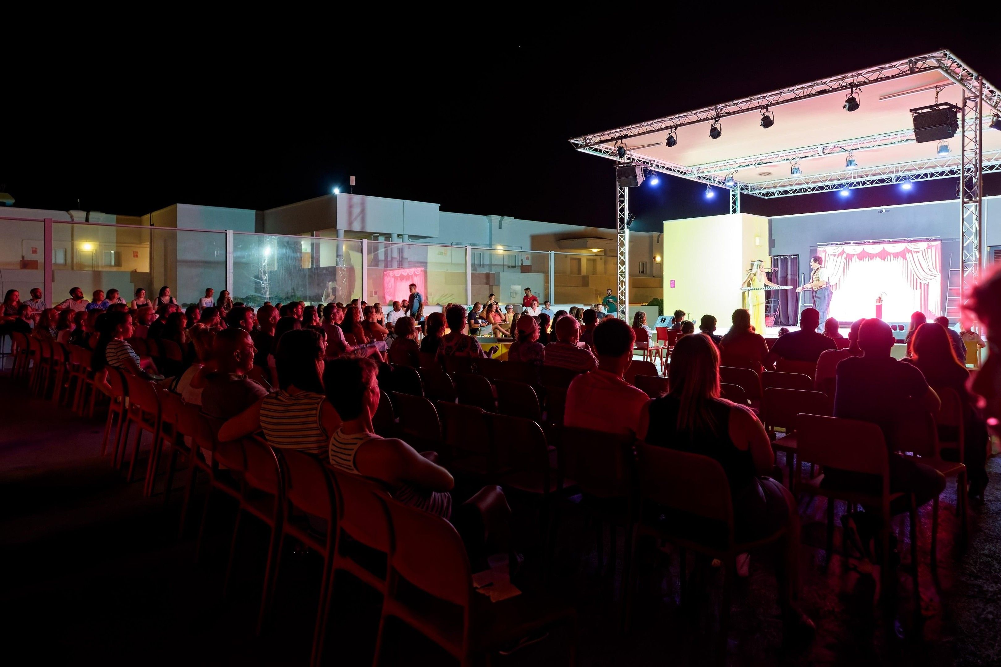 Eine Open-Air-Veranstaltung mit einer Bühne und einem Publikum, das auf Stühlen sitzt.