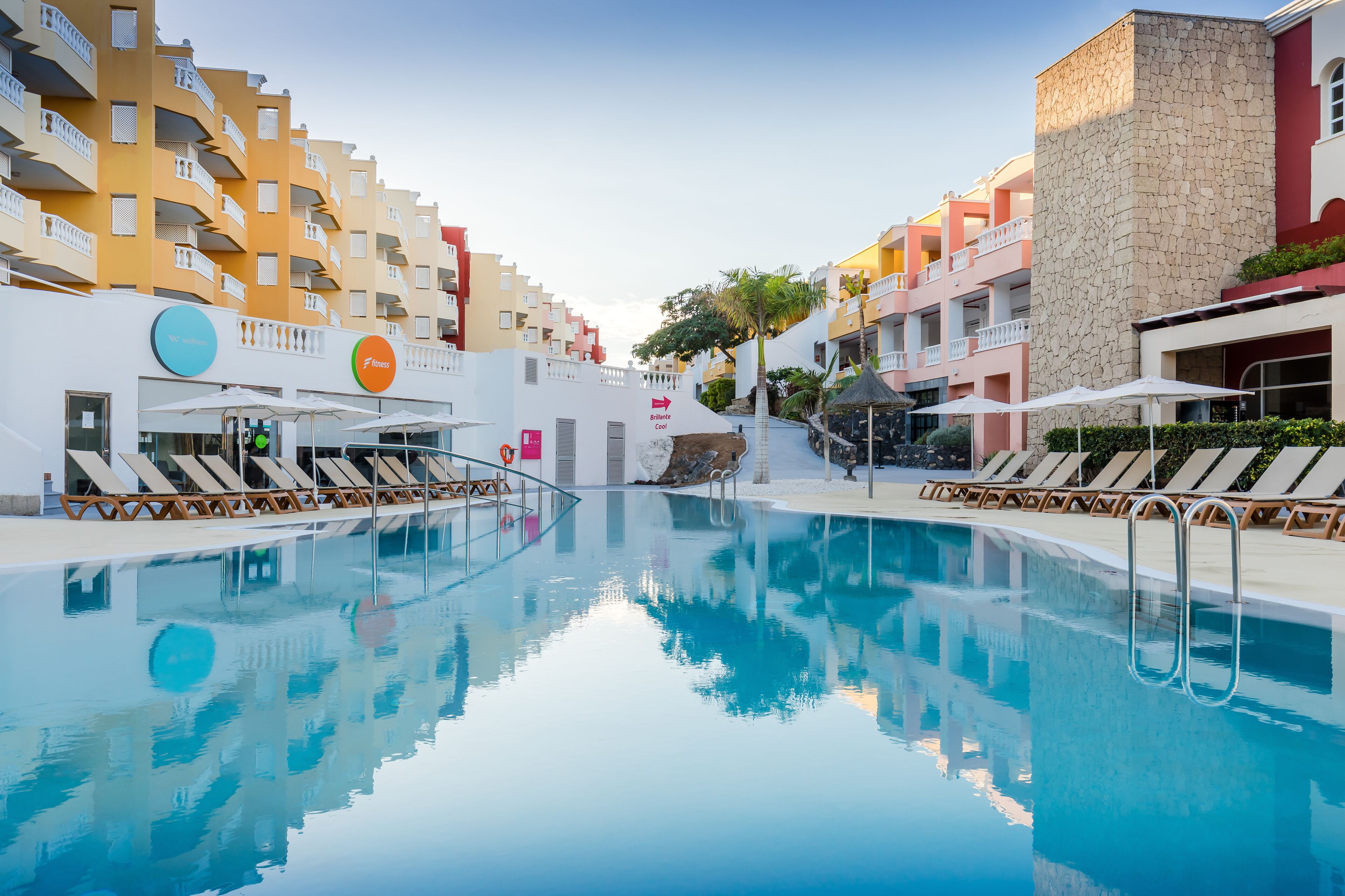 Una piscina con tumbonas y sombrillas, rodeada de edificios de varios pisos con balcones.