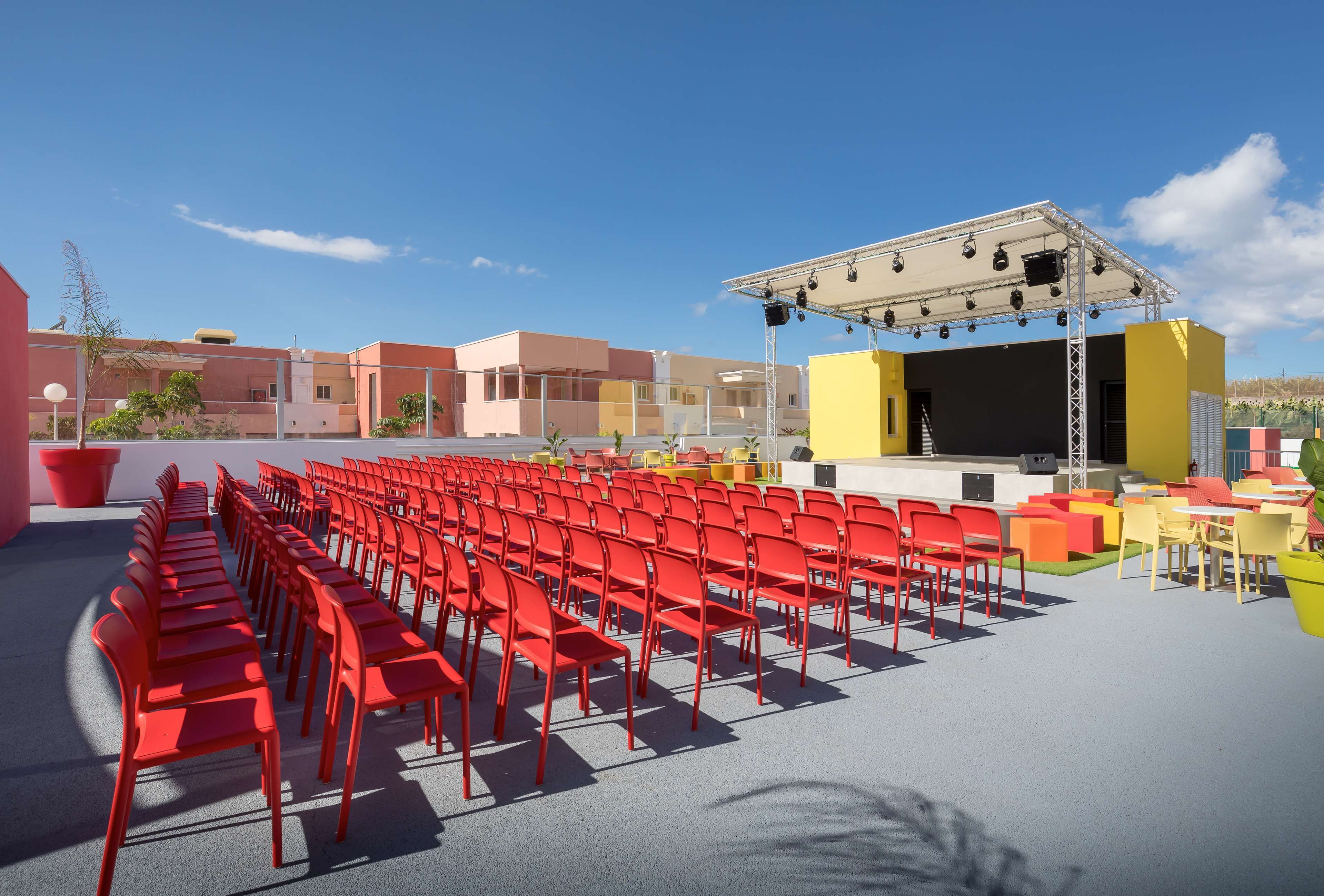 A stage with a backdrop and seating area with red chairs.