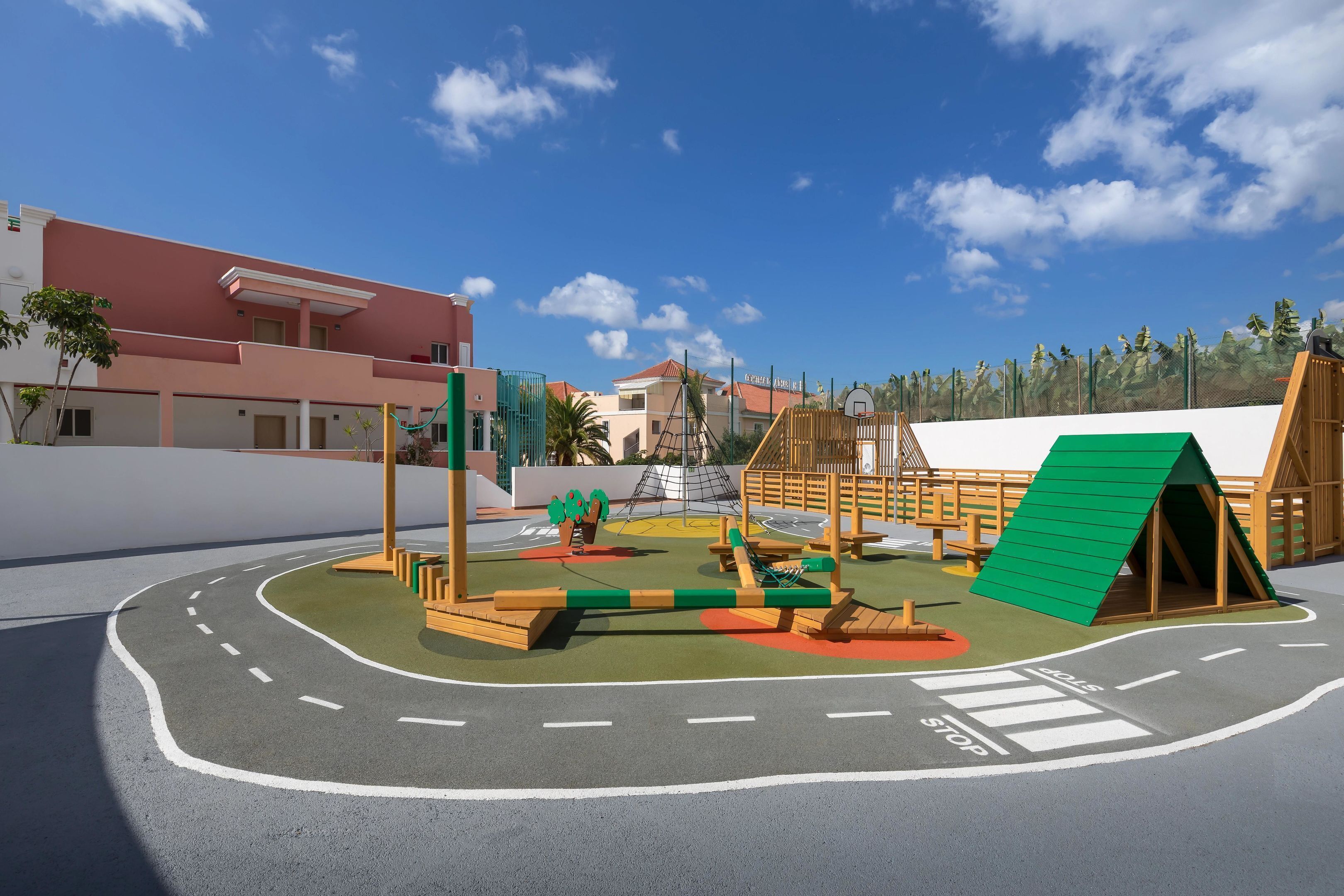 Un parc infantil amb diferents zones de jocs, un cèrcol de bàsquet i una tanca.