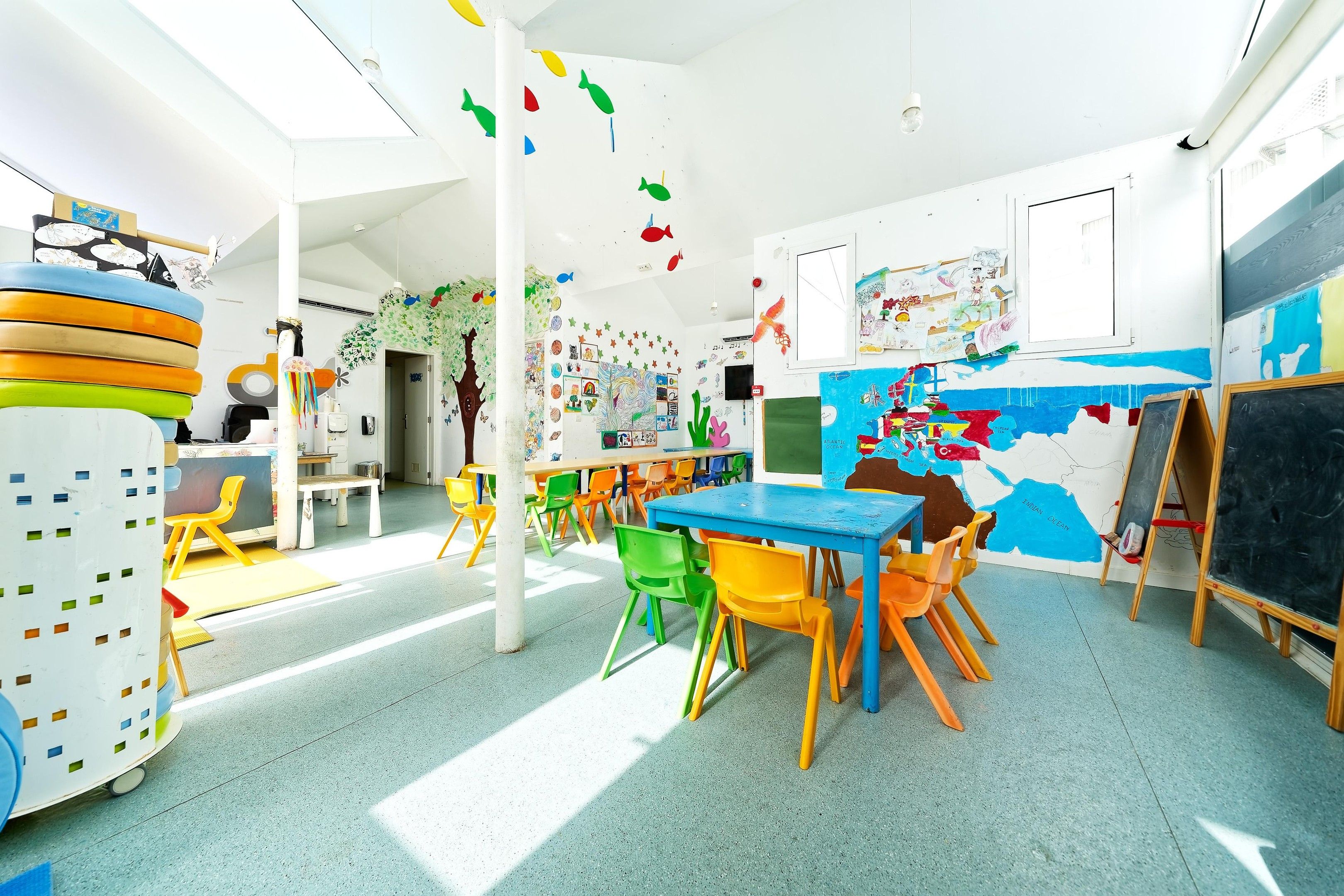 Un aula con sillas de colores, una mesa azul y carteles educativos en las paredes.