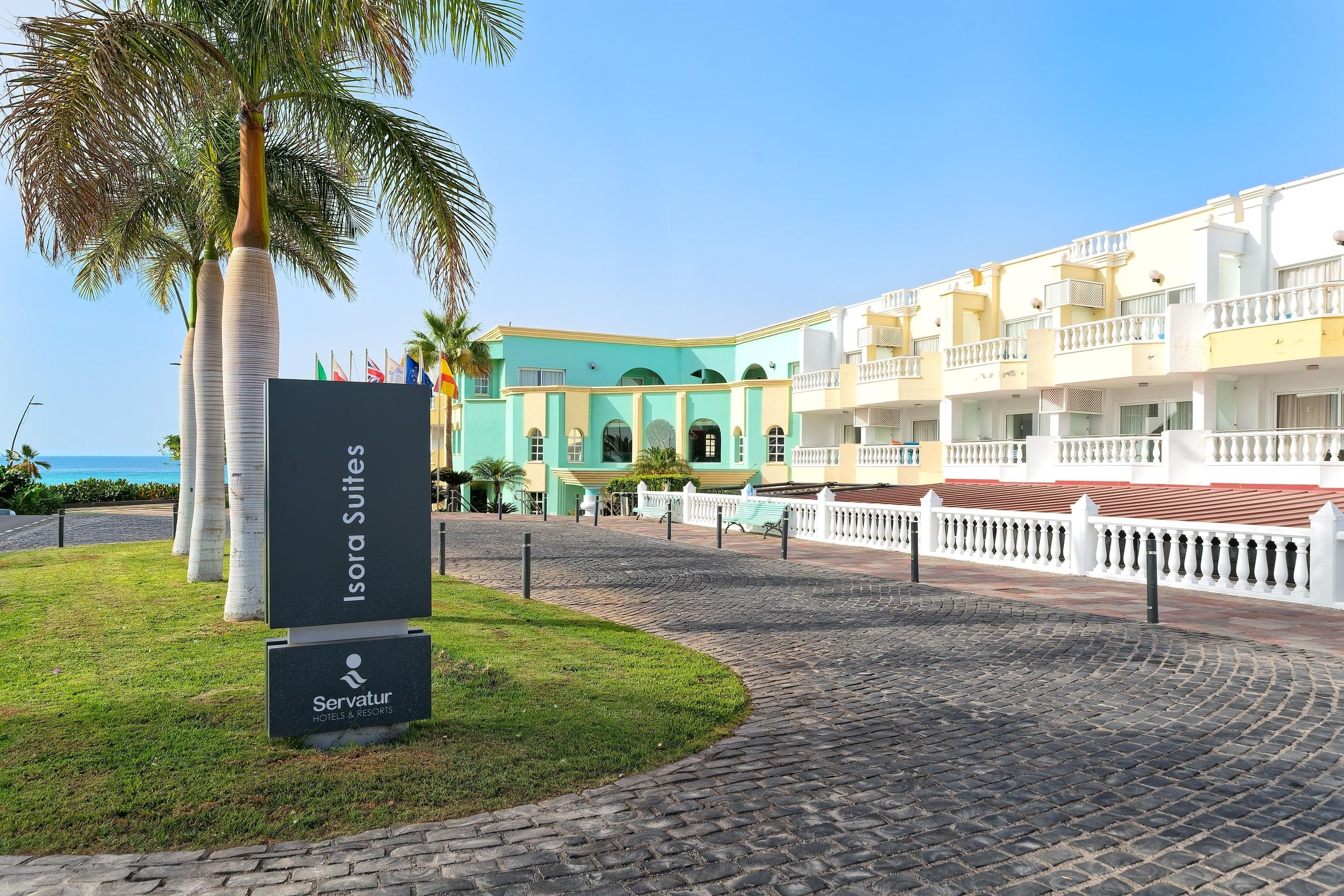 A hotel entrance with a sign for Isora Suites, a paved walkway, and a building with balconies.