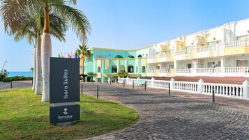 A hotel entrance with a sign for Isora Suites, a paved walkway, and a building with balconies.