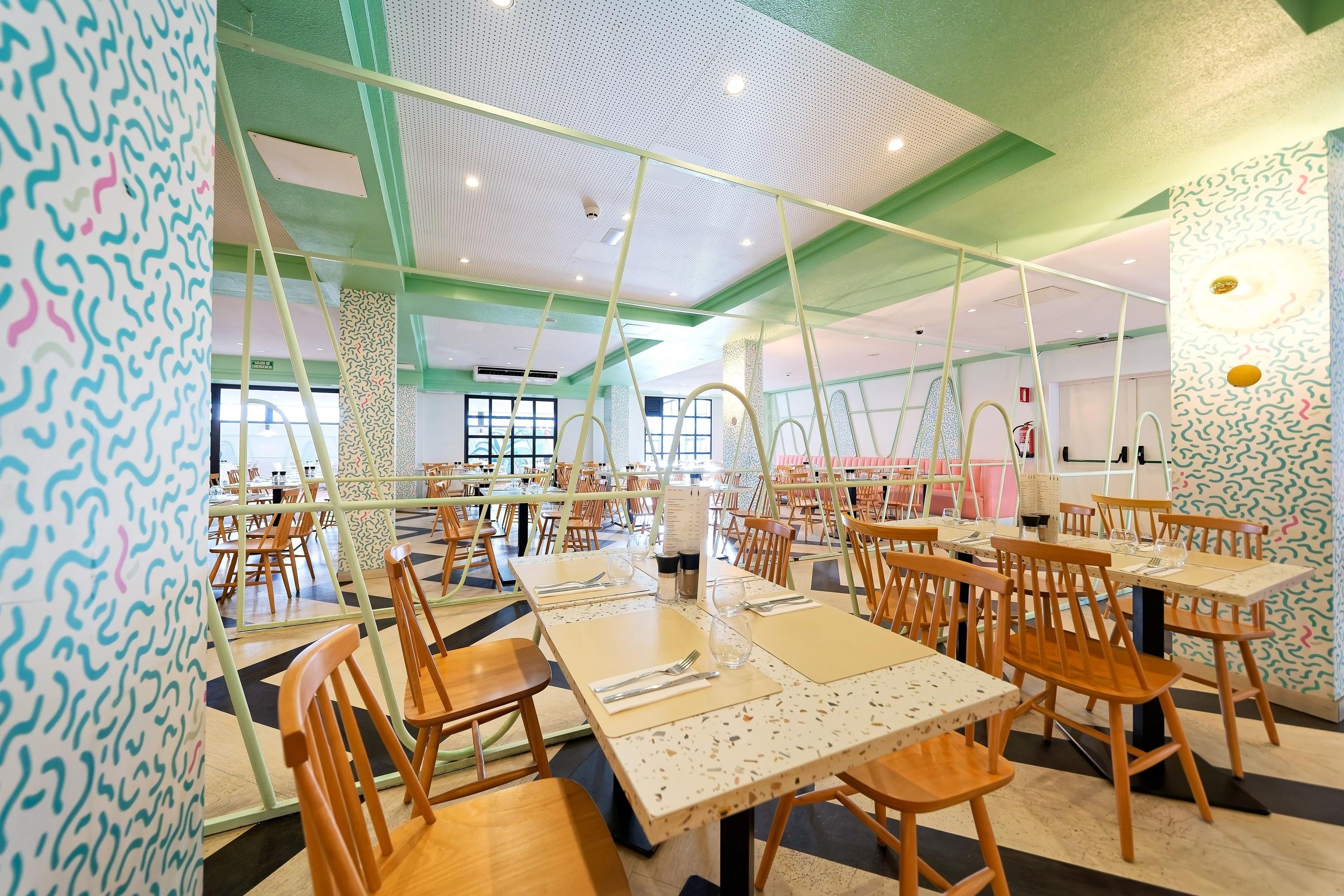 A spacious dining area with multiple tables and chairs, a high ceiling with a unique pattern, and a green and white color scheme.