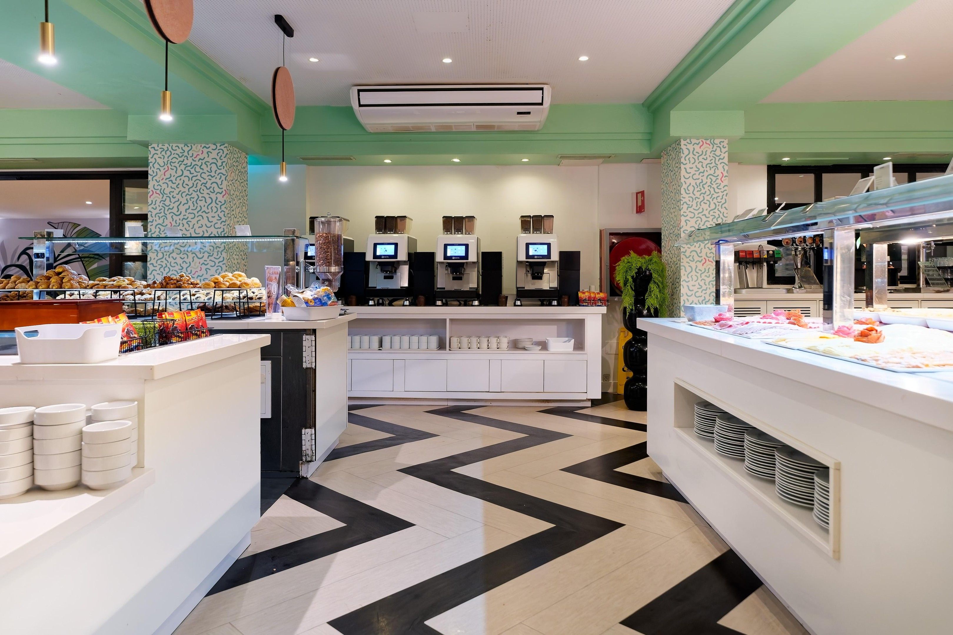Interior de cafeteria moderna amb un mostrador central, diverses màquines de cafè i un paviment amb un disseny original.
