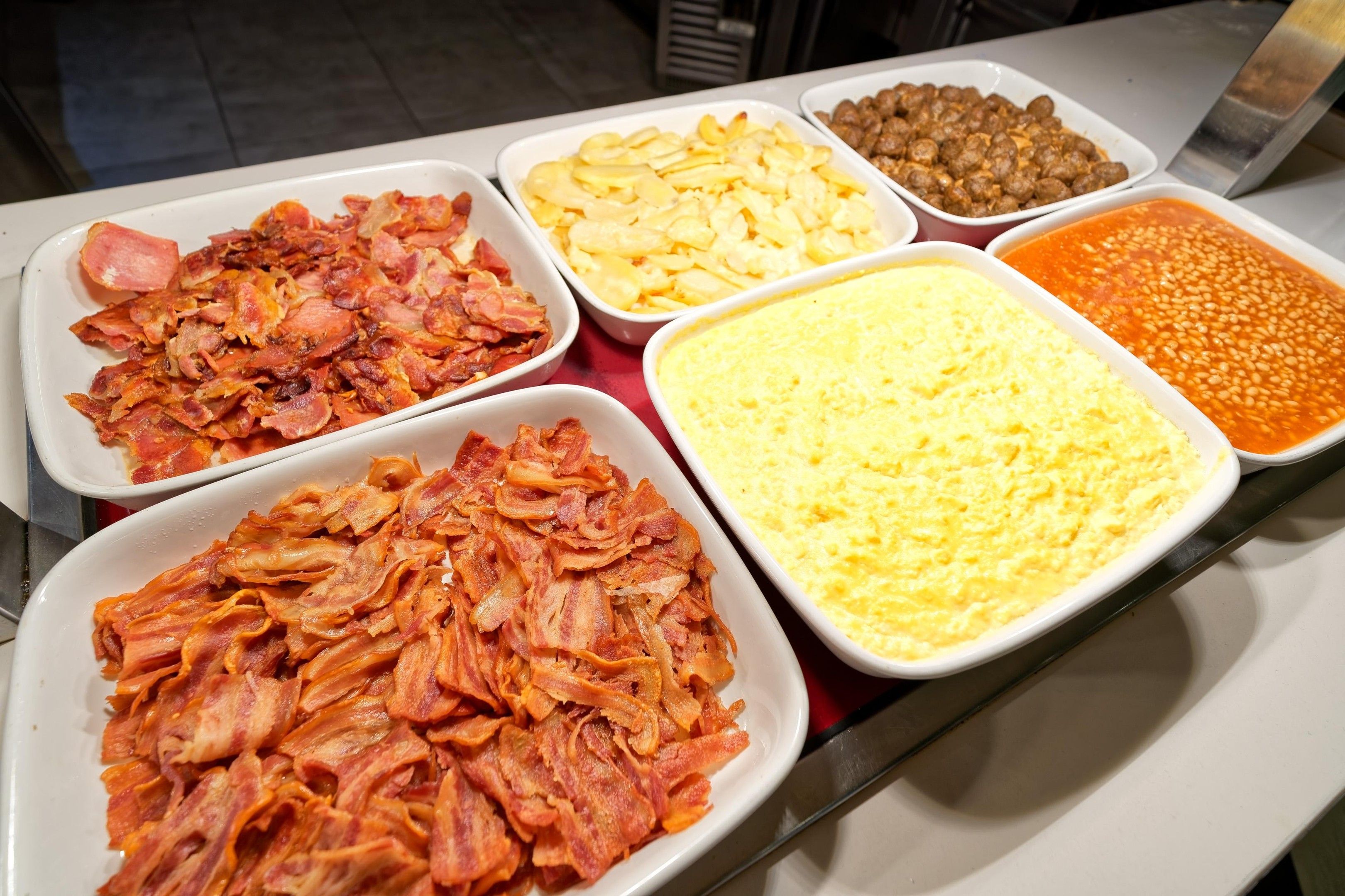 Un bufé con diferentes opciones de comida, incluyendo tocino, huevos y frijoles.