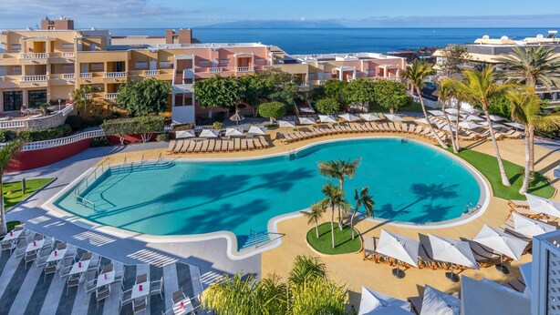 Un resort con una piscina grande, tumbonas y vista al mar.