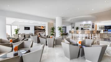 A modern hotel lobby with seating areas, a bar, and a large window with a cityscape view.