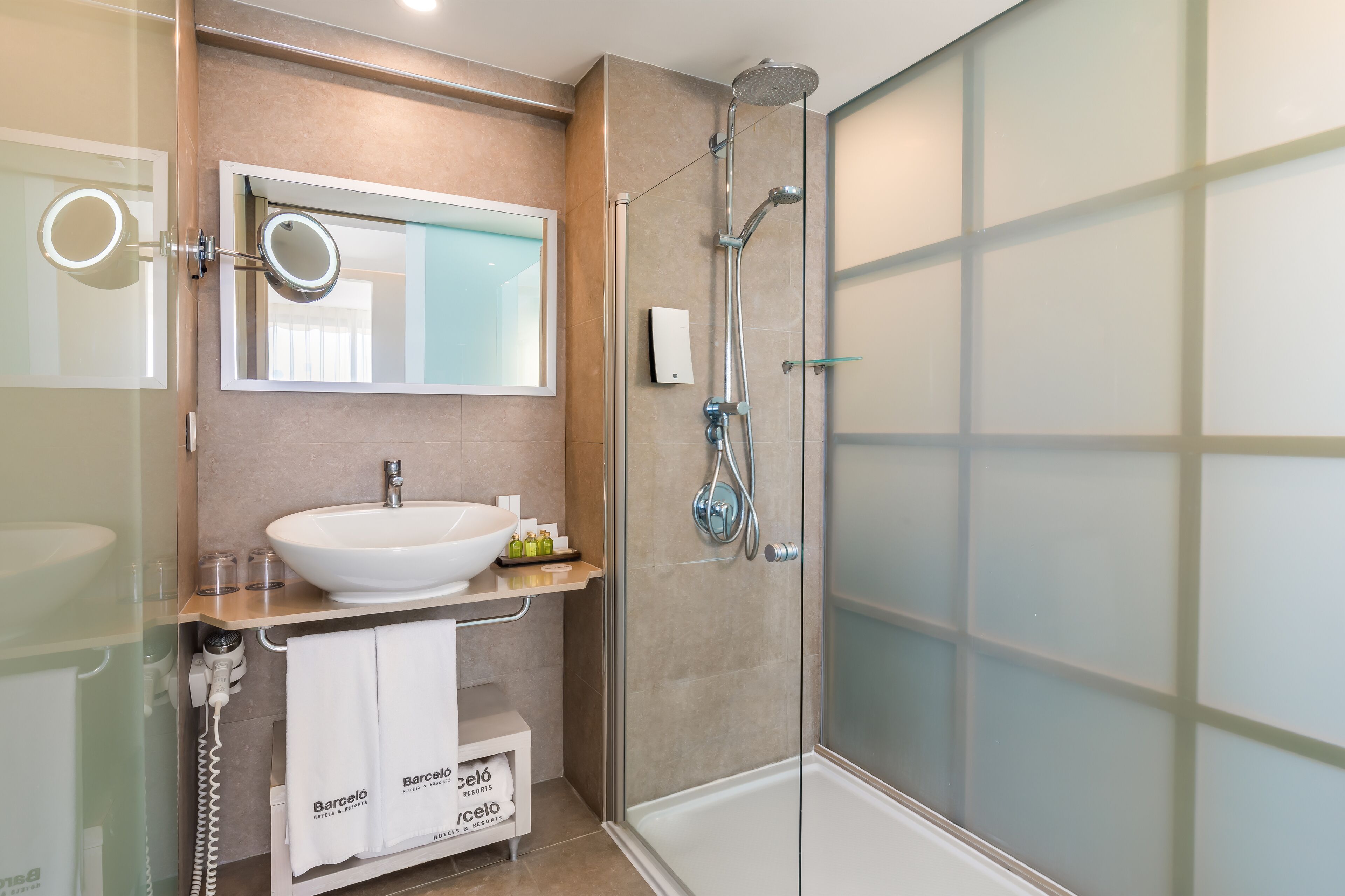 Un baño moderno con ducha envuelta en vidrio, un lavabo blanco y un espejo con un espejo redondo encima.