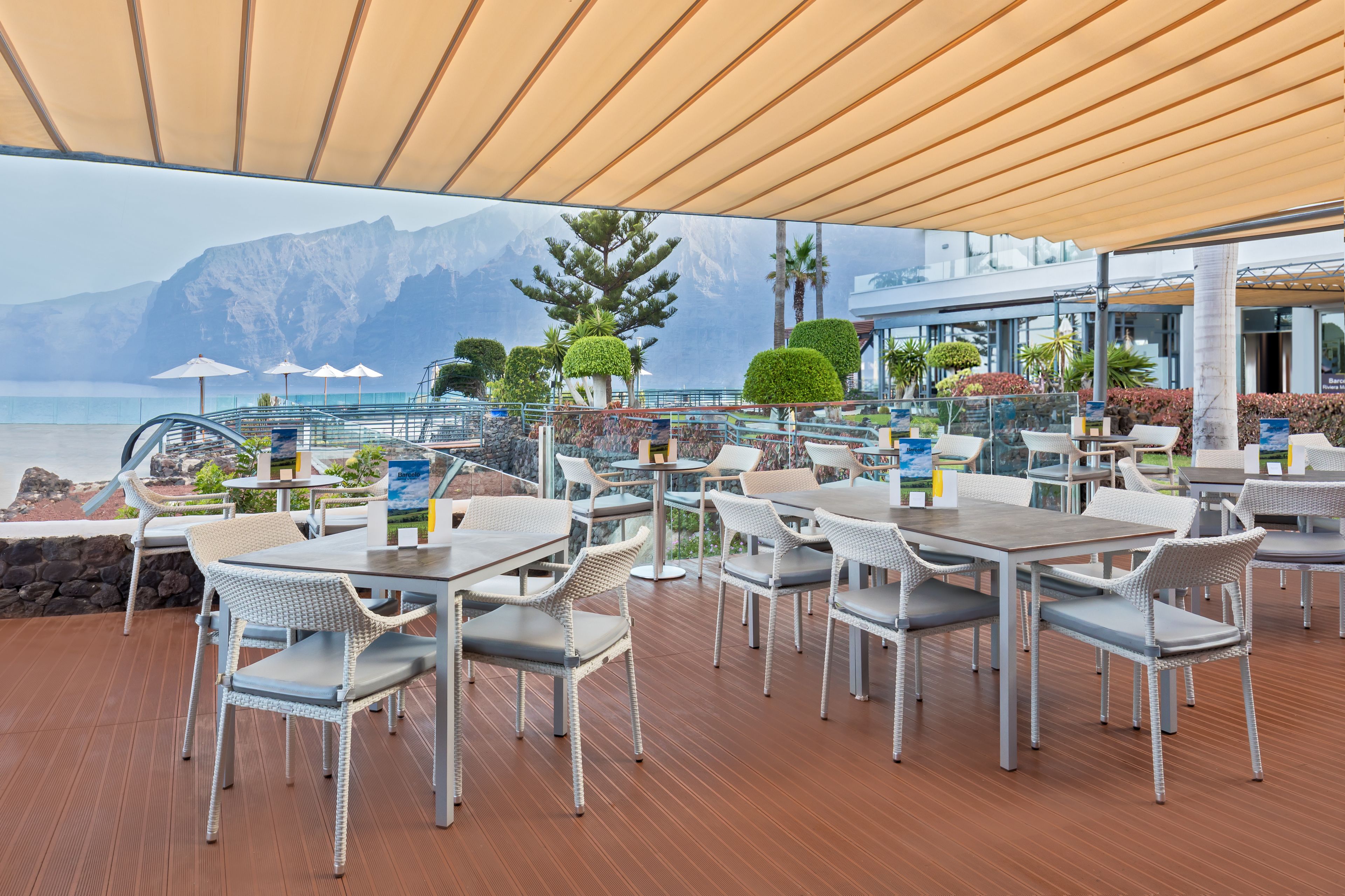 Un espacio de comedor al aire libre con mesas y sillas, con vistas a un cuerpo de agua y montañas.