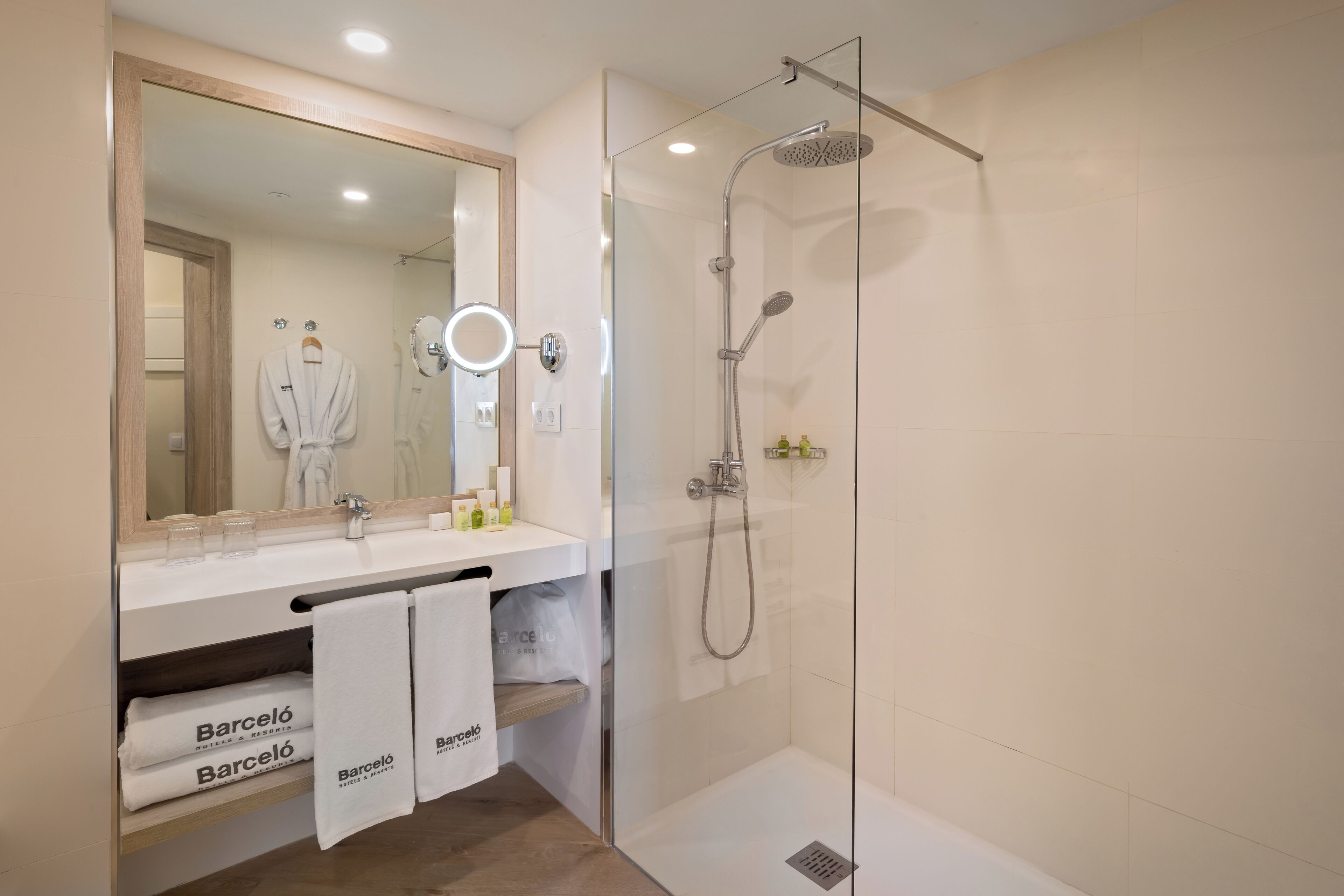 A modern bathroom with a glass-enclosed shower, a large mirror with a ring light, and a vanity with a towel rack holding two towels.
