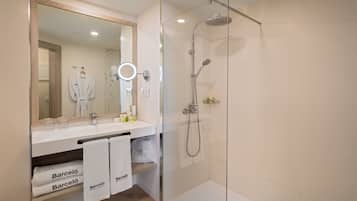 A modern bathroom with a glass-enclosed shower, a large mirror with a ring light, and a vanity with a towel rack holding two towels.