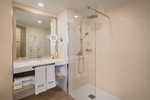 A modern bathroom with a glass-enclosed shower, a large mirror with a ring light, and a vanity with a towel rack holding two towels.