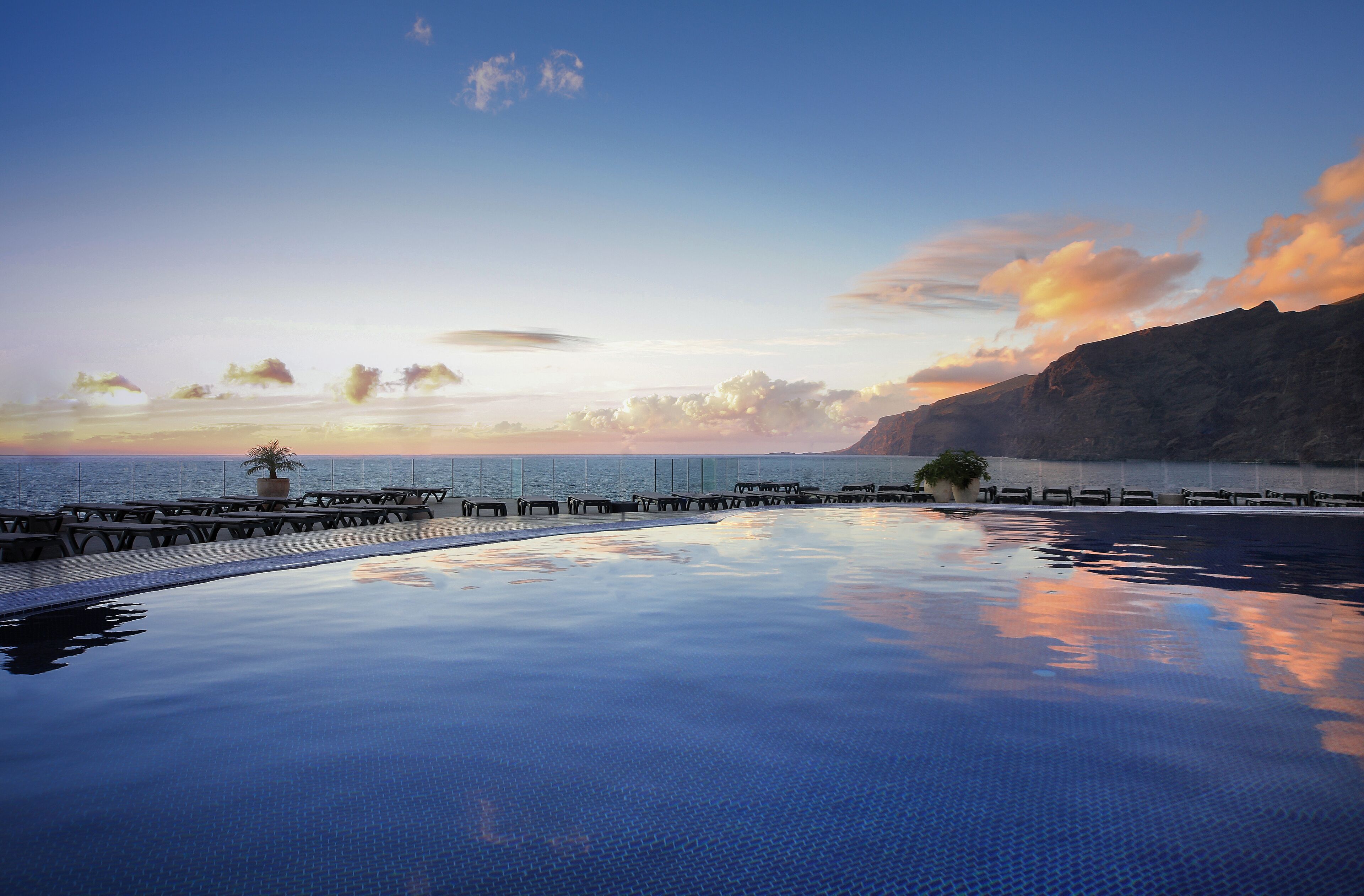 A serene infinity pool with a clear view of the ocean and a sunset.