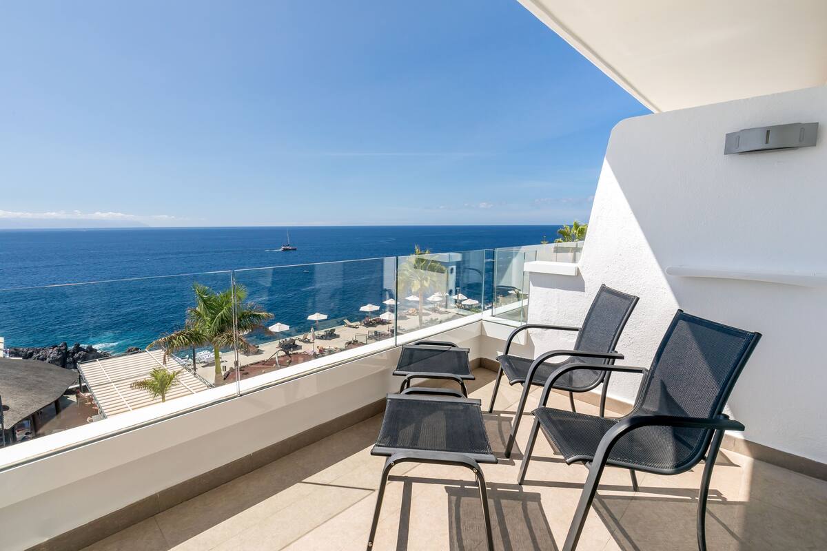 A balcony with a view of the ocean, equipped with chairs and a table.