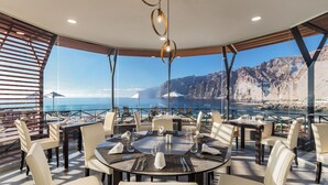 A dining area with round tables, white chairs, and a view of the sea and cliffs. - Barceló Santiago - Adults Only (Santiago del Teide)