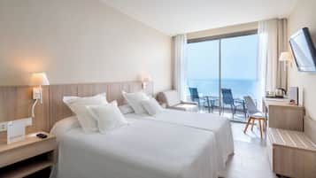 Habitación de hotel con dos camas, un escritorio, una silla, un televisor y vistas al mar.