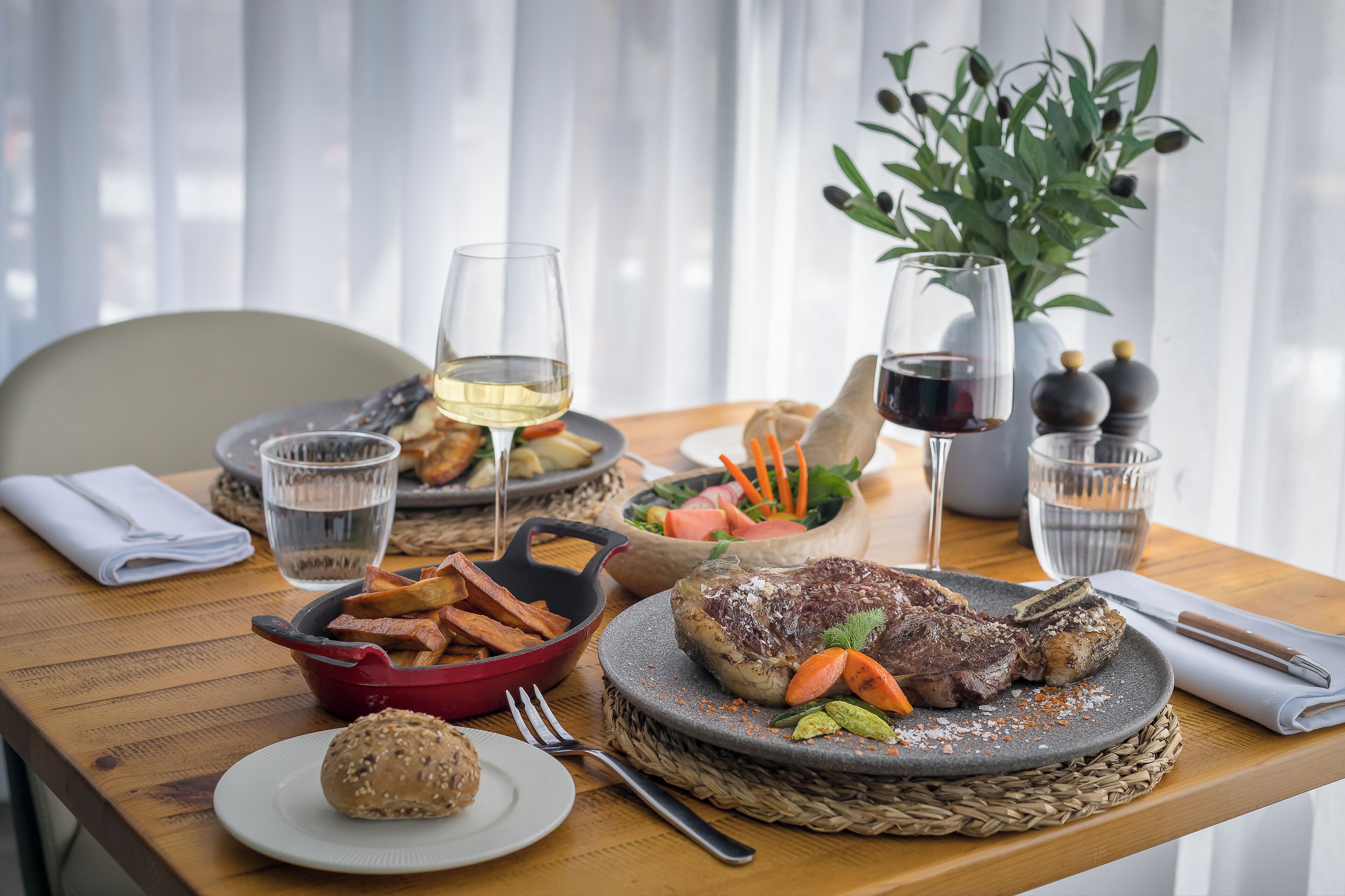 A dining table with a variety of dishes including steak, fries, and salad, along with glasses of water and wine.