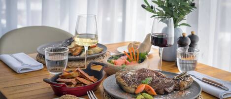 Una mesa de comedor con una variedad de platos, incluyendo bistec, papas fritas y ensalada, además de vasos de agua y vino.