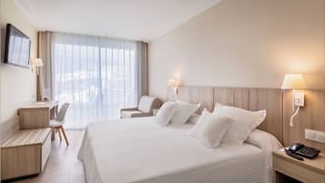 A hotel room with a large bed, a desk with a chair, a TV mounted on the wall, and a window with curtains.