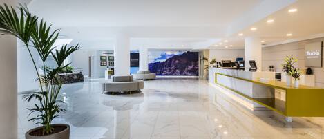 A modern hotel lobby with a marble floor, a reception desk, and a large wall mural.