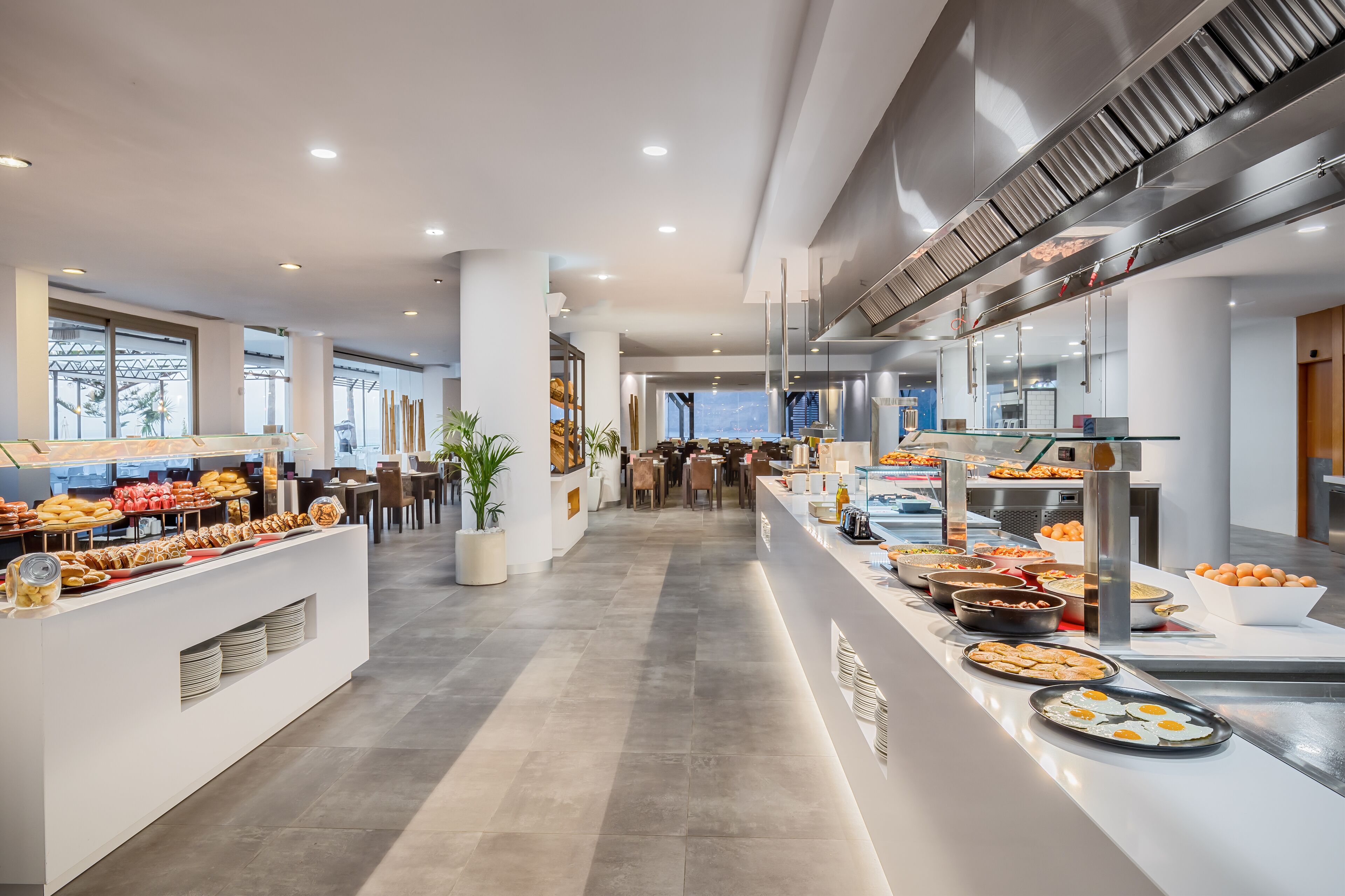 A modern hotel lobby with a long buffet line, seating area, and large windows offering a view of the city.