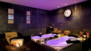 A spa room with two large tubs, a clock, and candles.