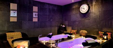 A spa room with two large tubs, a clock, and candles.