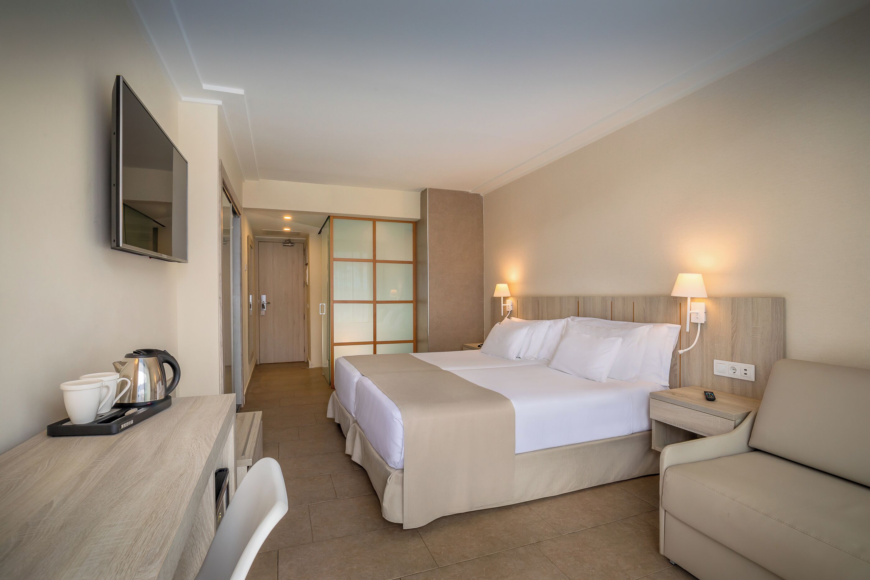 Habitación de hotel con cama, mesita de noche, l ámpara y televisor montado en la pared.