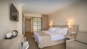 Una habitación de hotel con una cama, un escritorio con hervidor, una silla y una mesita de noche con lámpara.