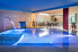 Un área de piscina interior moderna con una fuente de agua cristalina, una estatua y una zona de estar con una pared de cristal.