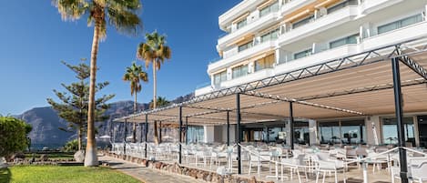 A resort with outdoor seating, palm trees, and a view of the ocean.
