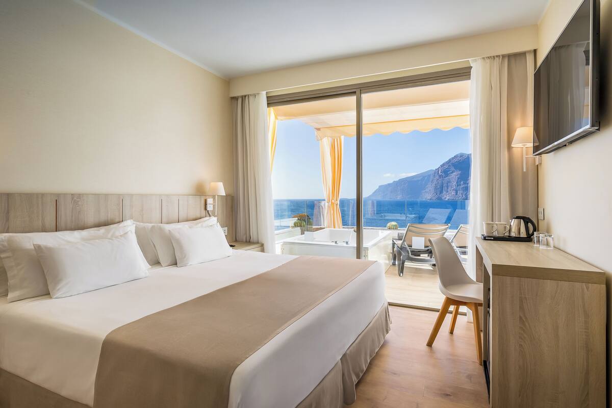A hotel room with a large bed, a desk, and a view of the sea.