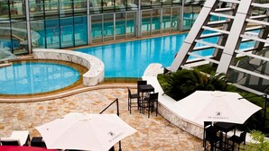 A rooftop pool area with a glass enclosure, lounge chairs, and a red seating area.