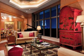 Un salón amplio con un gran ventanal, un piano de cola y un aparador rojo con diseños intrincados.