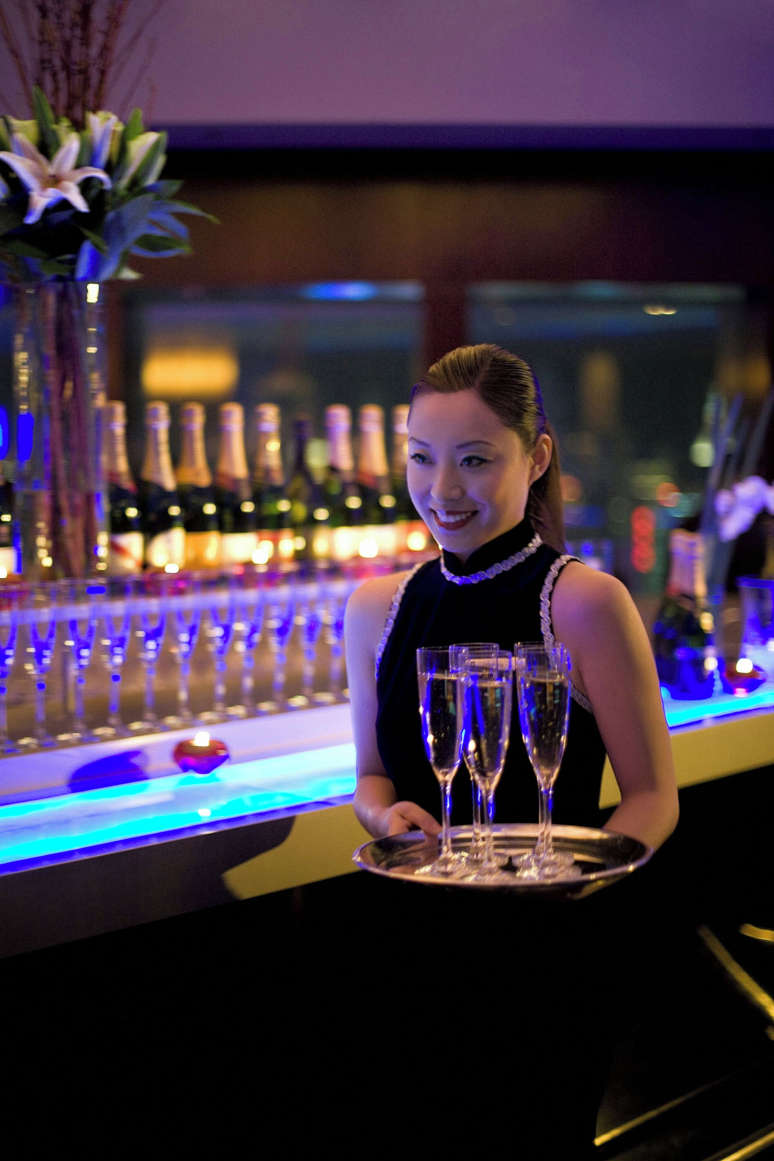 A bar area with a bartender holding a tray of glasses.