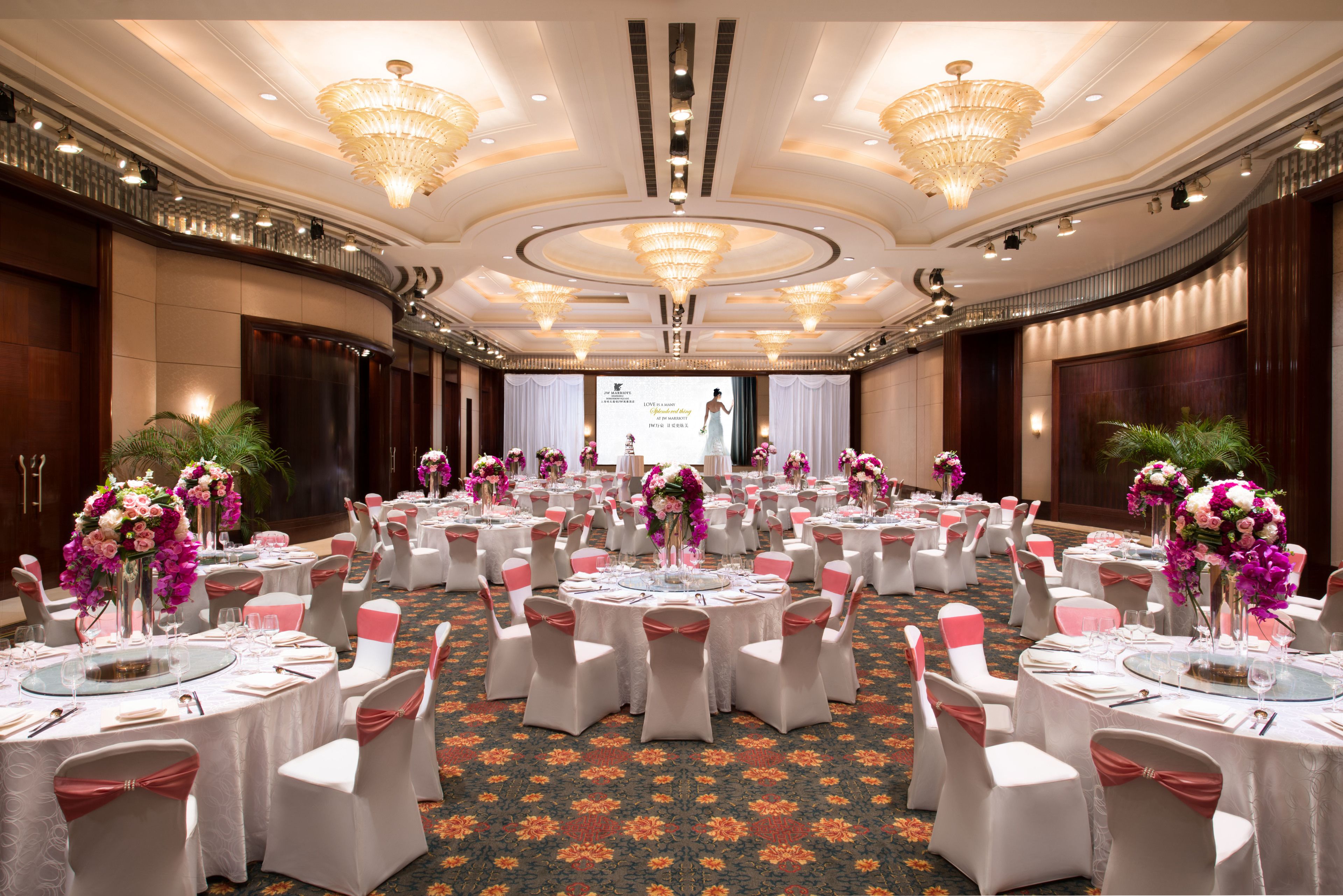 A banquet hall with round tables, white tablecloths, and pink sashes.