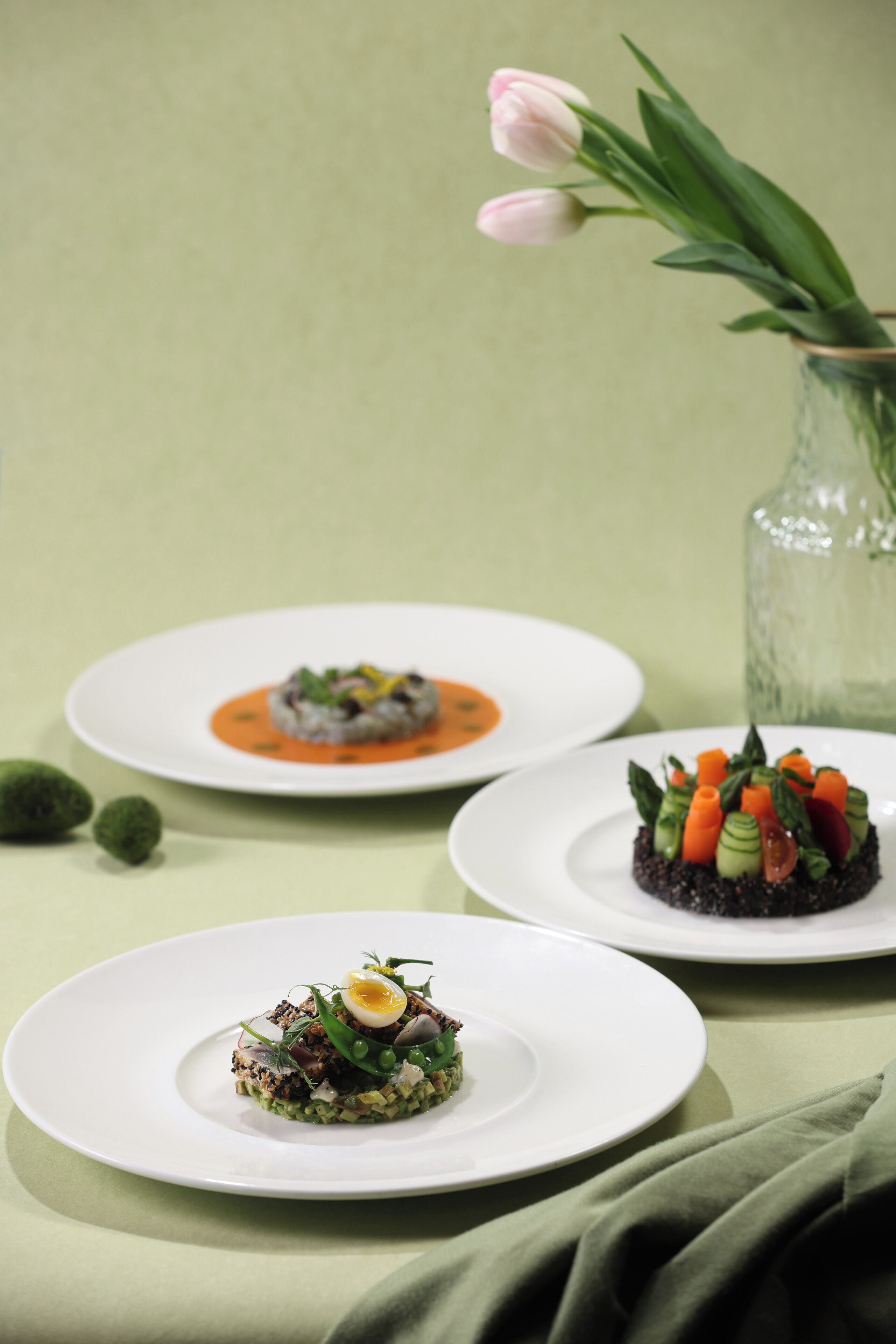 Tres platos de comida sobre una mesa, con un jarrón de flores al fondo.