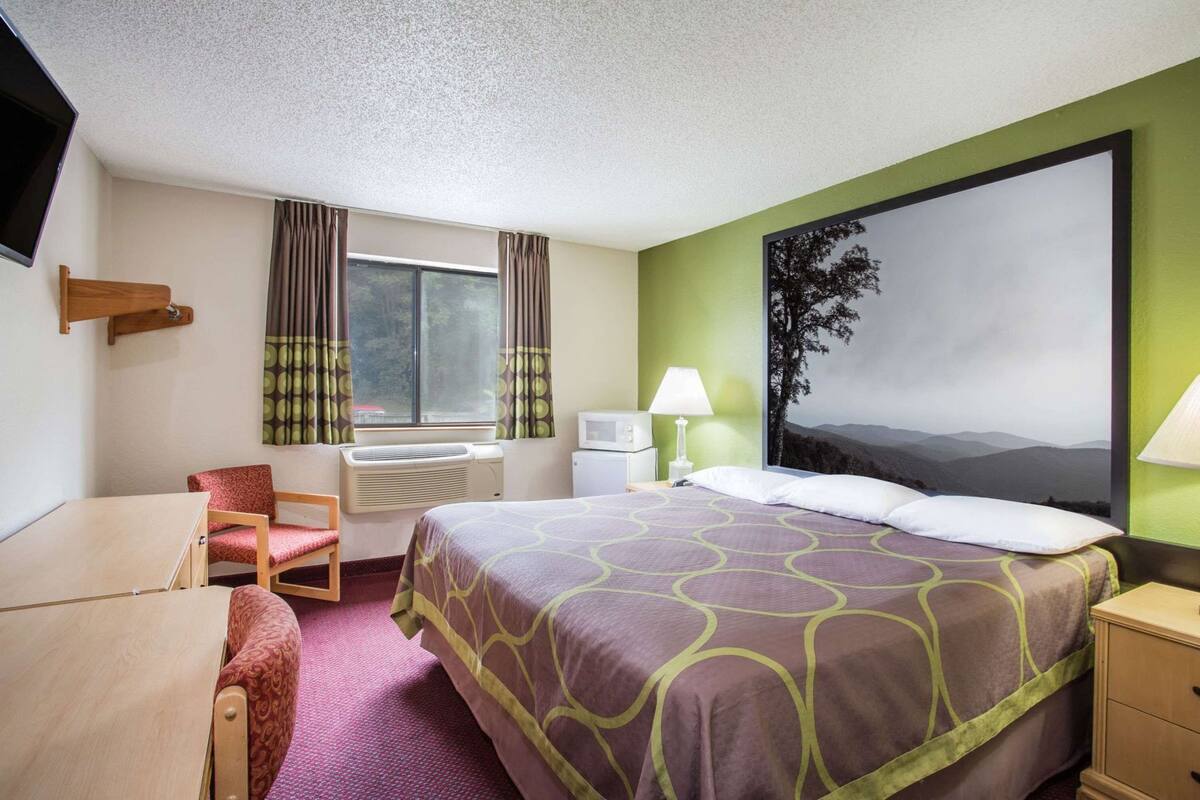 Une chambre d’hôtel avec un lit, un bureau, une chaise et une grande fenêtre avec des rideaux.