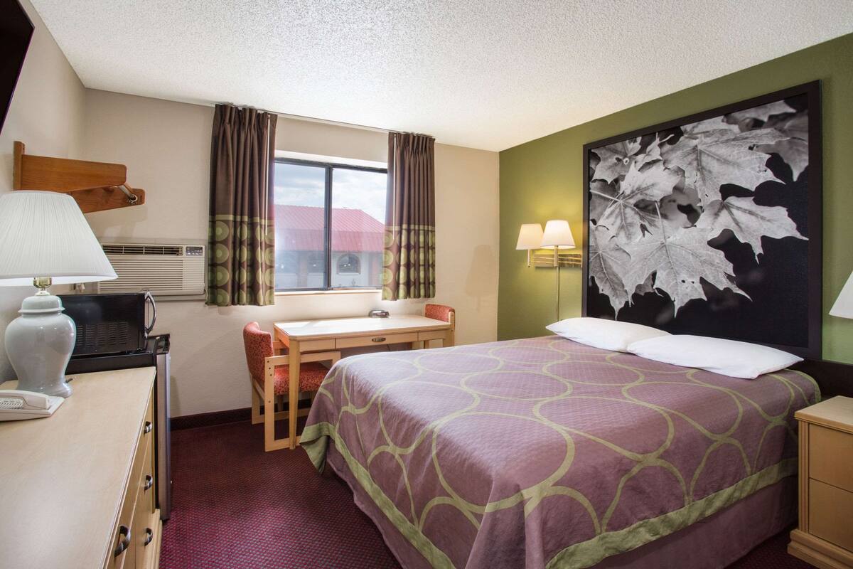 Une chambre d’hôtel avec un lit, un bureau, une chaise et une grande fenêtre avec des rideaux.
