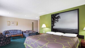 A hotel room with a large bed, two armchairs, a small table, and a painting on the wall.