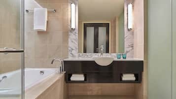 A modern bathroom with a glass-enclosed shower, a white bathtub, a marble-tiled vanity with a sink, and a large mirror.