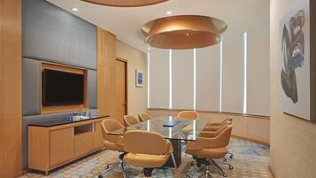 A conference room with a glass table, swivel chairs, a flat-screen TV, wooden cabinets, and a patterned carpet.