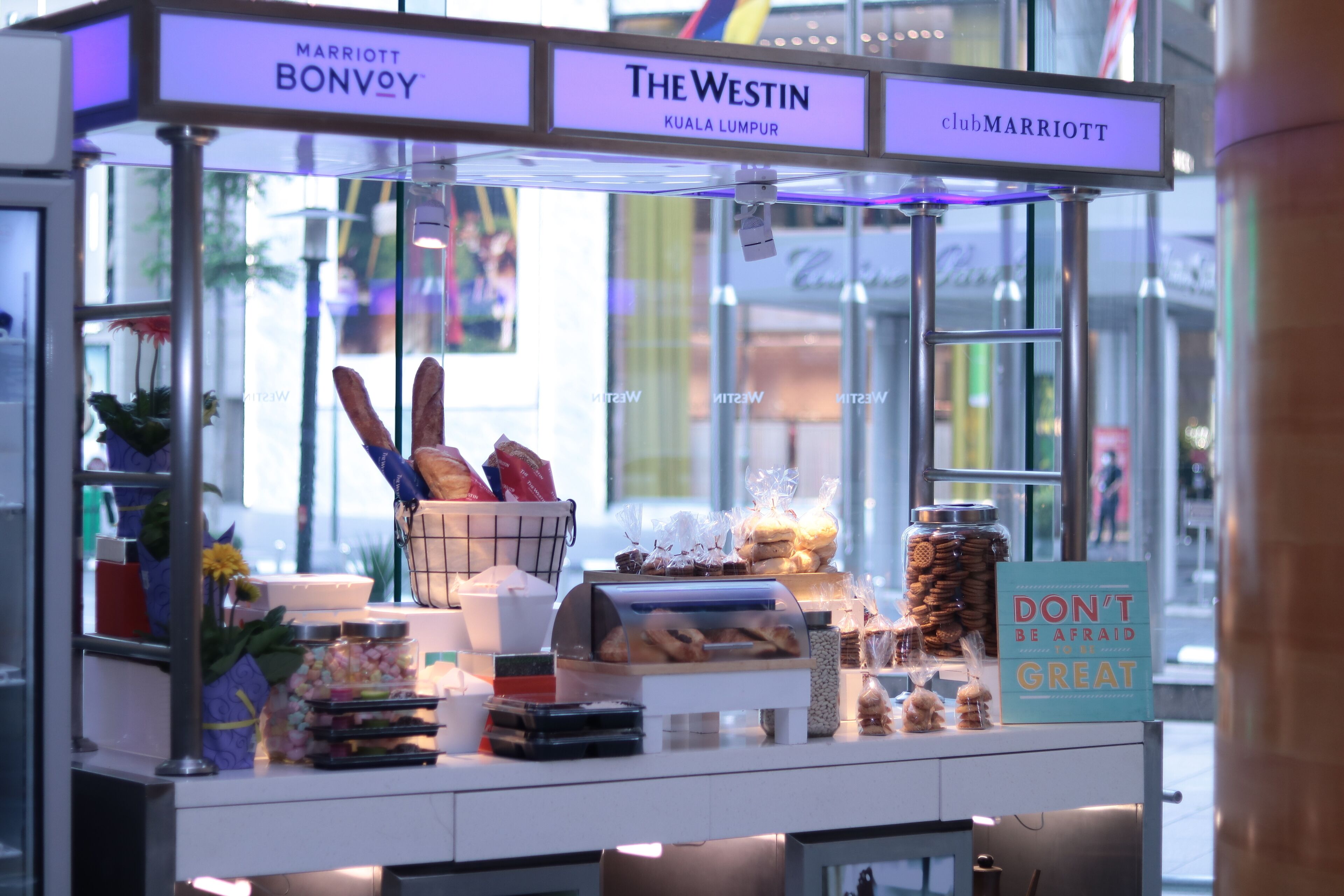 A food kiosk with a sign reading "DON'T BE AFRAID TO BE GREAT" and "The Westin Kuala Lumpur."